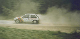 A rally car going through a very dusty forest stage.